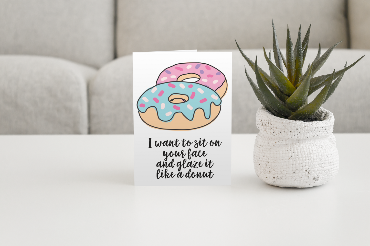White vertical greetings card featuring a colourful donut design. To the bottom it reads 'i want to sit on your face & glaze it like a donut'. Printed in black ink.