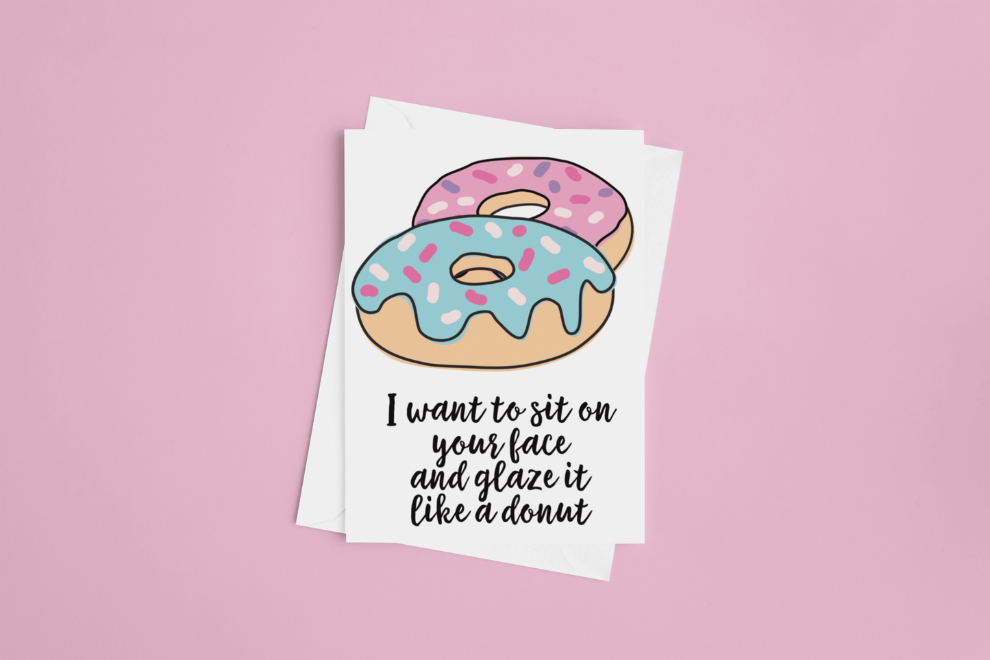 White vertical greetings card featuring a colourful donut design. To the bottom it reads 'i want to sit on your face & glaze it like a donut'. Printed in black ink.