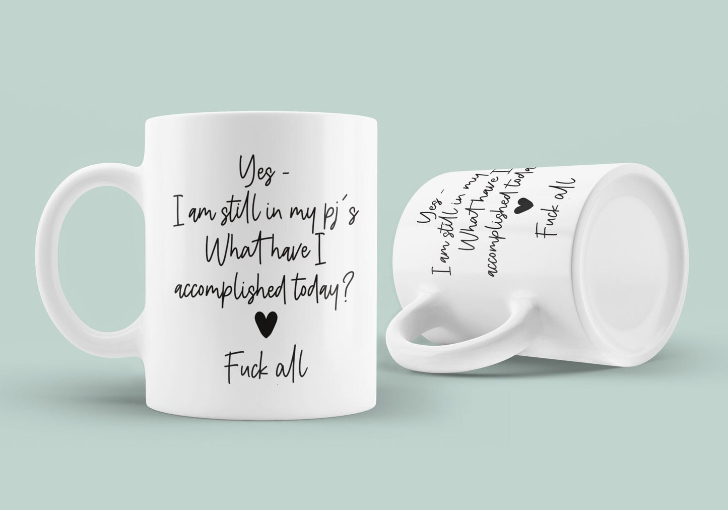 A white ceramic mug featuring the funny quote ‘yes i'm still in my pj's. What have i accomplished today? Fuck all’. Printed in black ink with a black heart.