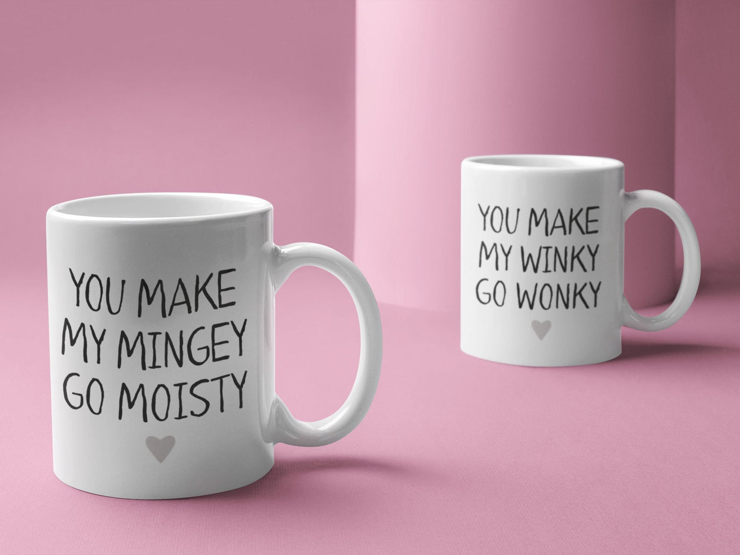 A pair of white ceramic mug featuring the funny quotes you make my mingey go moisty and you make my winky go wonky. Printed in black ink with a grey heart to the bottom centre of the design.
