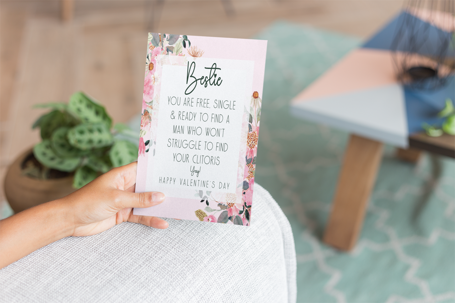 White card with a pink floral design to the front. In the middle has a funny message that reads 'bestie, you are single & ready to find a man who won't struggle to find your clitoris. Yay, happy valentine's day'. Printed in black ink.