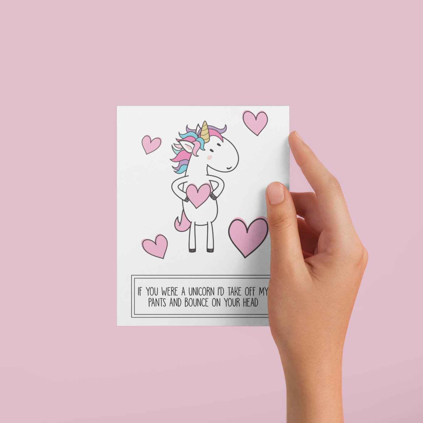 Hand holding a vertical greetings card featuring a fun unicorn design. To the botton it reads 'if you were a unicorn, i'd take off my pants & bounce on your head'. Printed in black ink.