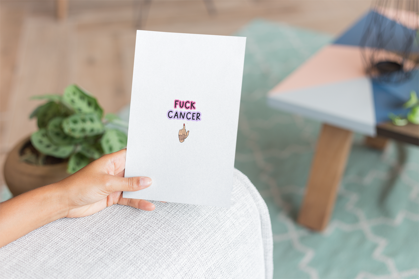 White vertical greetings card with a middle finger clipart in the centre. Above the middle finger design is the words 'fuck cancer', printed in black with a pink & purple outline.