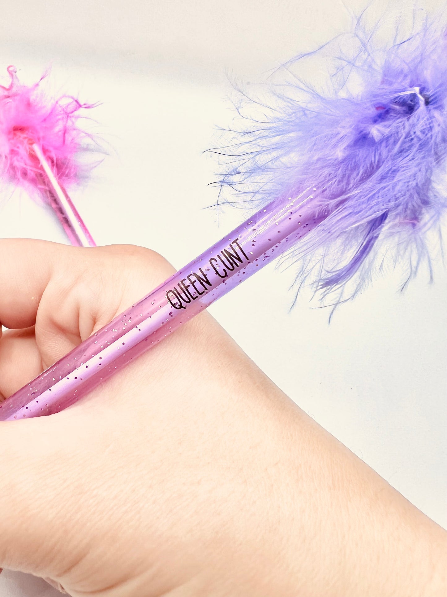 2 pack pens, pink and purple. Pink pen says 'cute but fucking vulgar' the purple says 'queen cunt'. Both pens have a glittery base, fluffy top and a plastic crown topper. Blue ink
