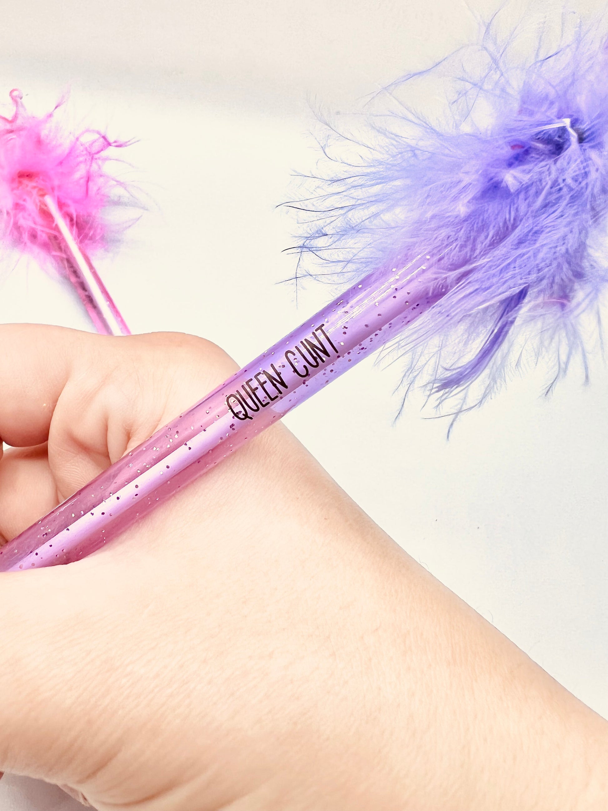 2 pack pens, pink and purple. Pink pen says 'cute but fucking vulgar' the purple says 'queen cunt'. Both pens have a glittery base, fluffy top and a plastic crown topper. Blue ink