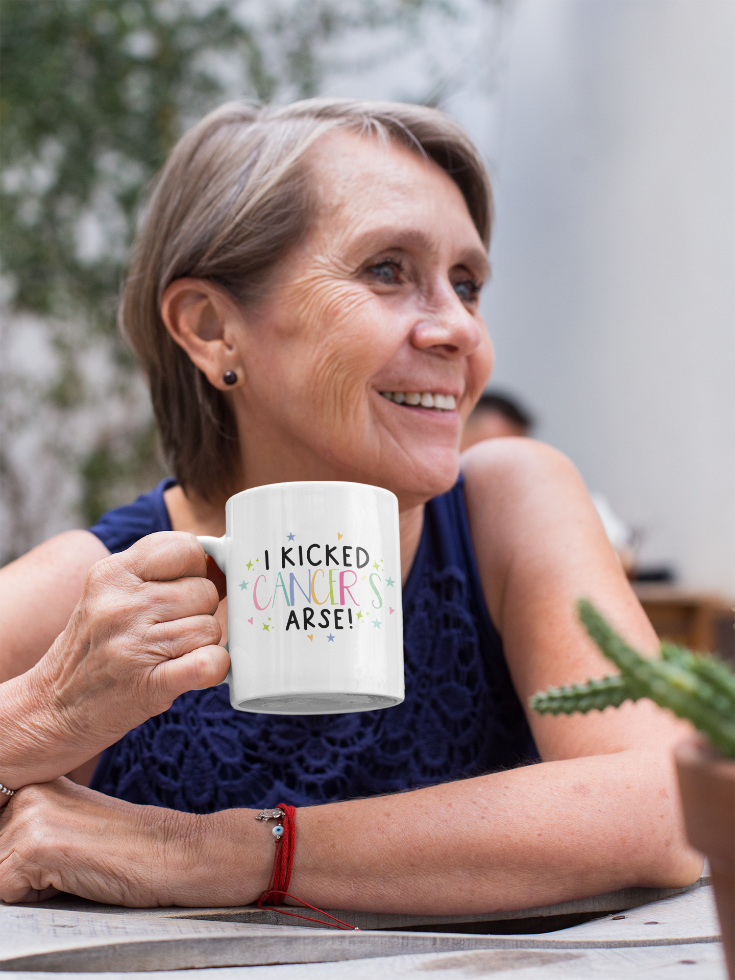 White mug with the words 'i kicked cancers arse! printed in the middle. Cancer is multicoloured pastel colours surrounded by little pastel stars & hearts.