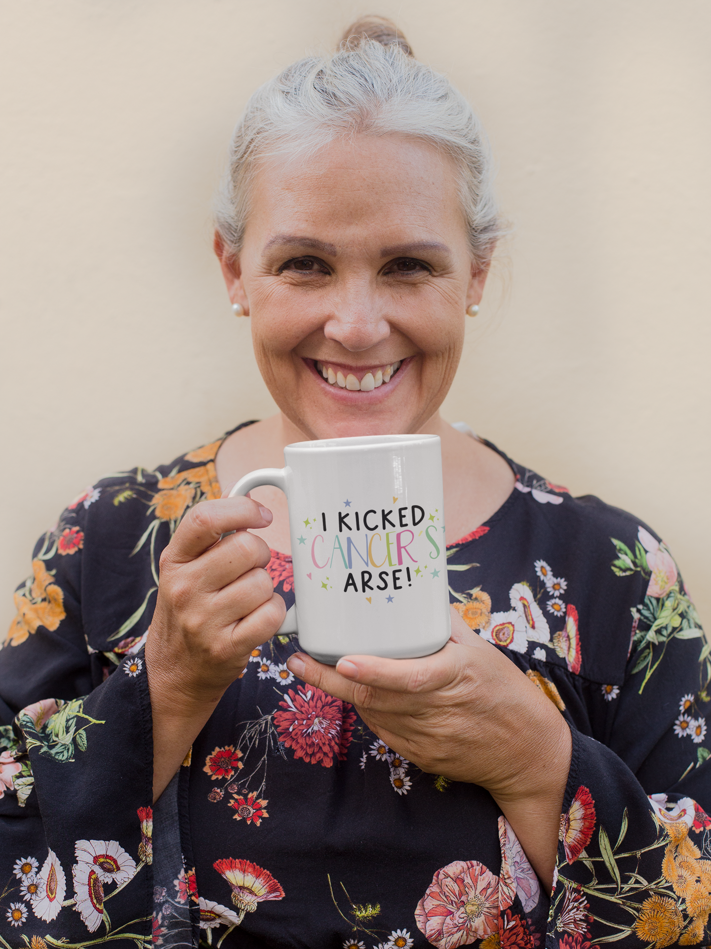 White mug with the words 'i kicked cancers arse!' printed in the middle. Cancer is multicoloured pastel colours surrounded by little pastel stars & hearts.