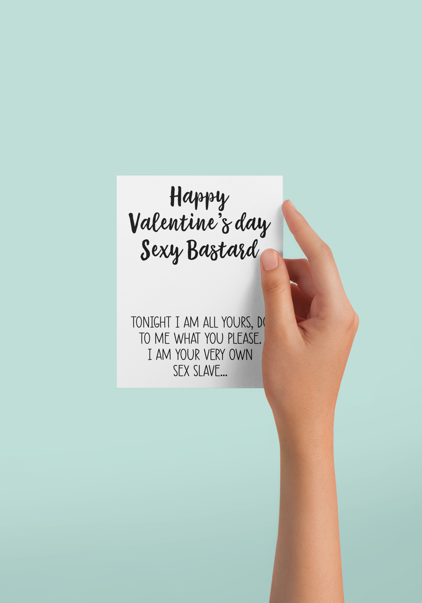 Girls hand holding a white vertical greetings card featuring a fun quote to the front 'happy Valentine's Day you sexy bastard' & a sex slave quote underneath. Printed in black ink.