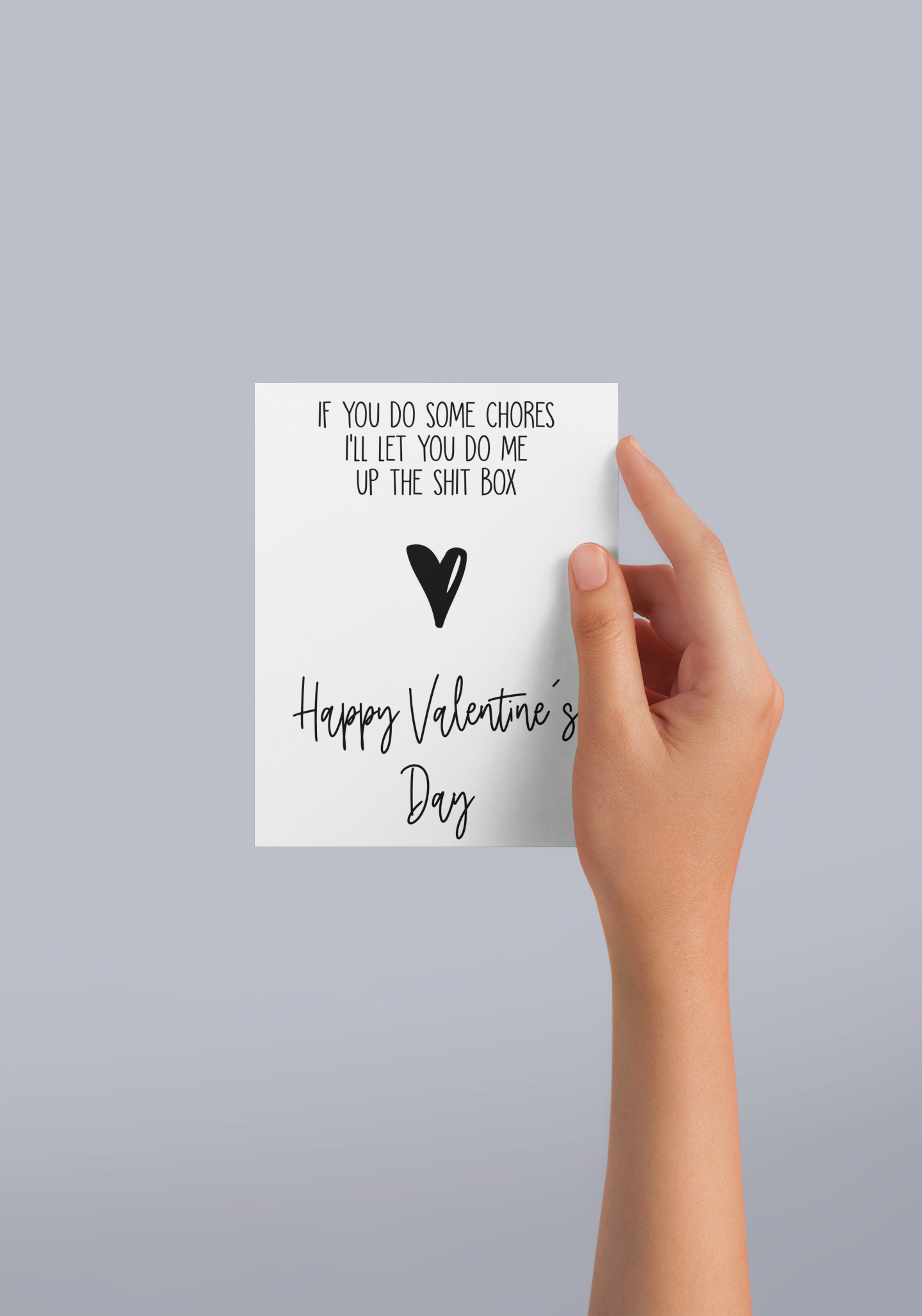 Girls hand holding a white vertical greetings card featuring a funny quote 'if you do some chores i'll let you do me up the shit box'. Underneath is a black heart and then 'happy Valentine's Day' printed to the bottom, all in black ink.White vertical Valentine's card with the quote if you do some chores i'll let you do me up the shit-box, with a black heart underneath, then it reads happy Valentine's day.