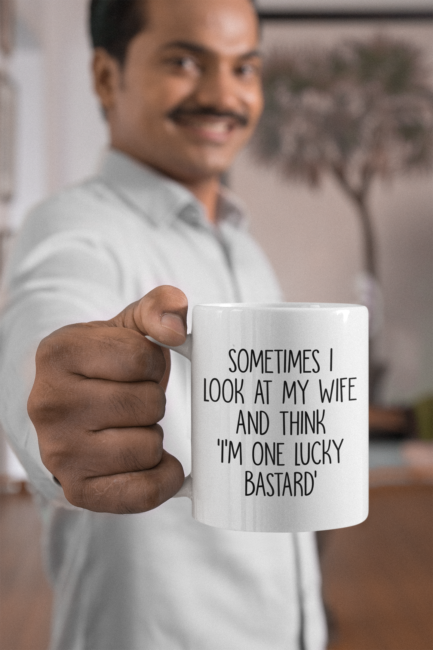Man holding a white mug with a funny quote 'sometimes i look at my wife and think i'm one lucky bastard''. Printed in black ink.