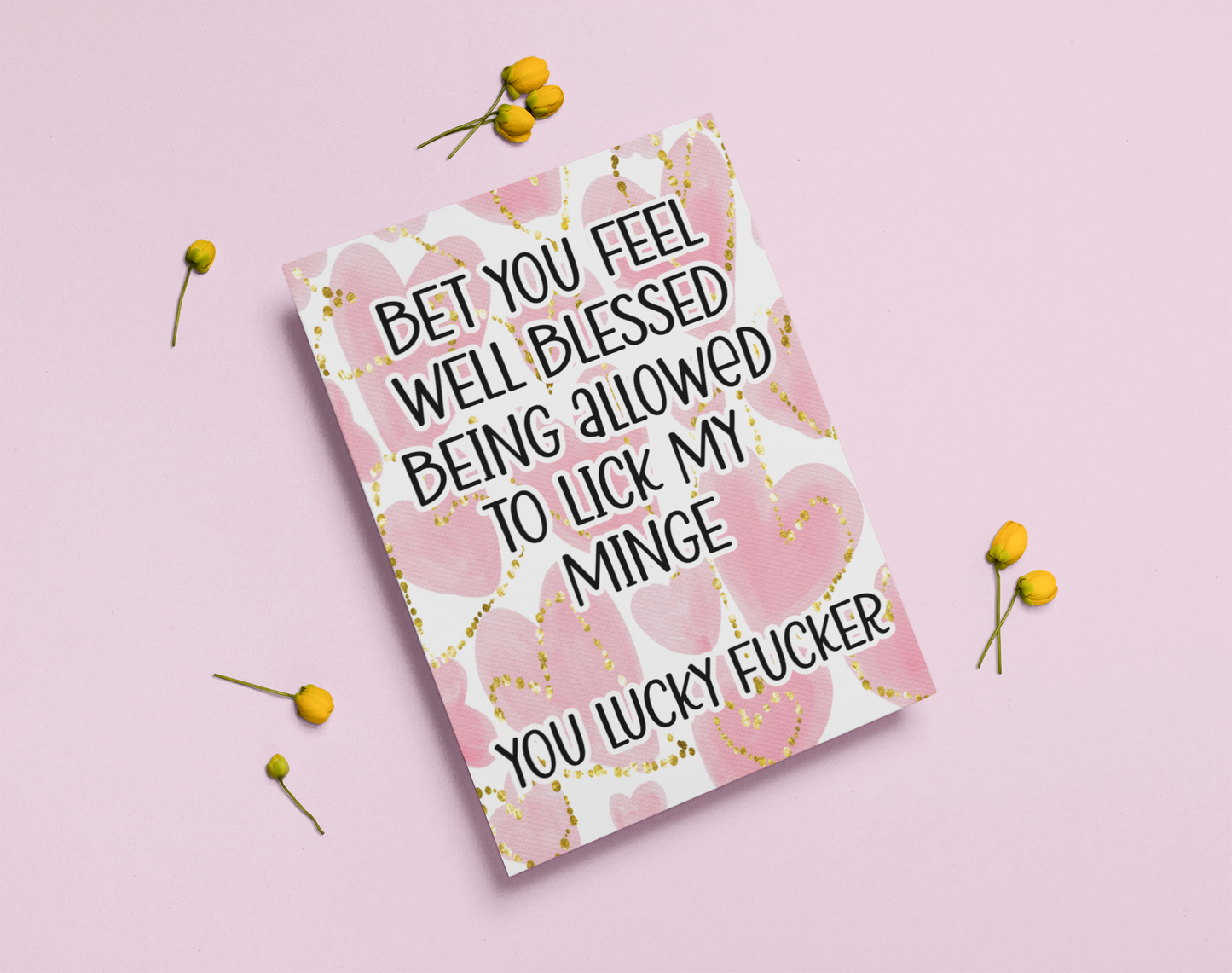 White vertical greetings card with a pink watercolour heart design to the front. Over the design is a funny quote 'bet you feel well blessed being allowed to lick my minge.. you lucky fucker'. Printed in back ink.