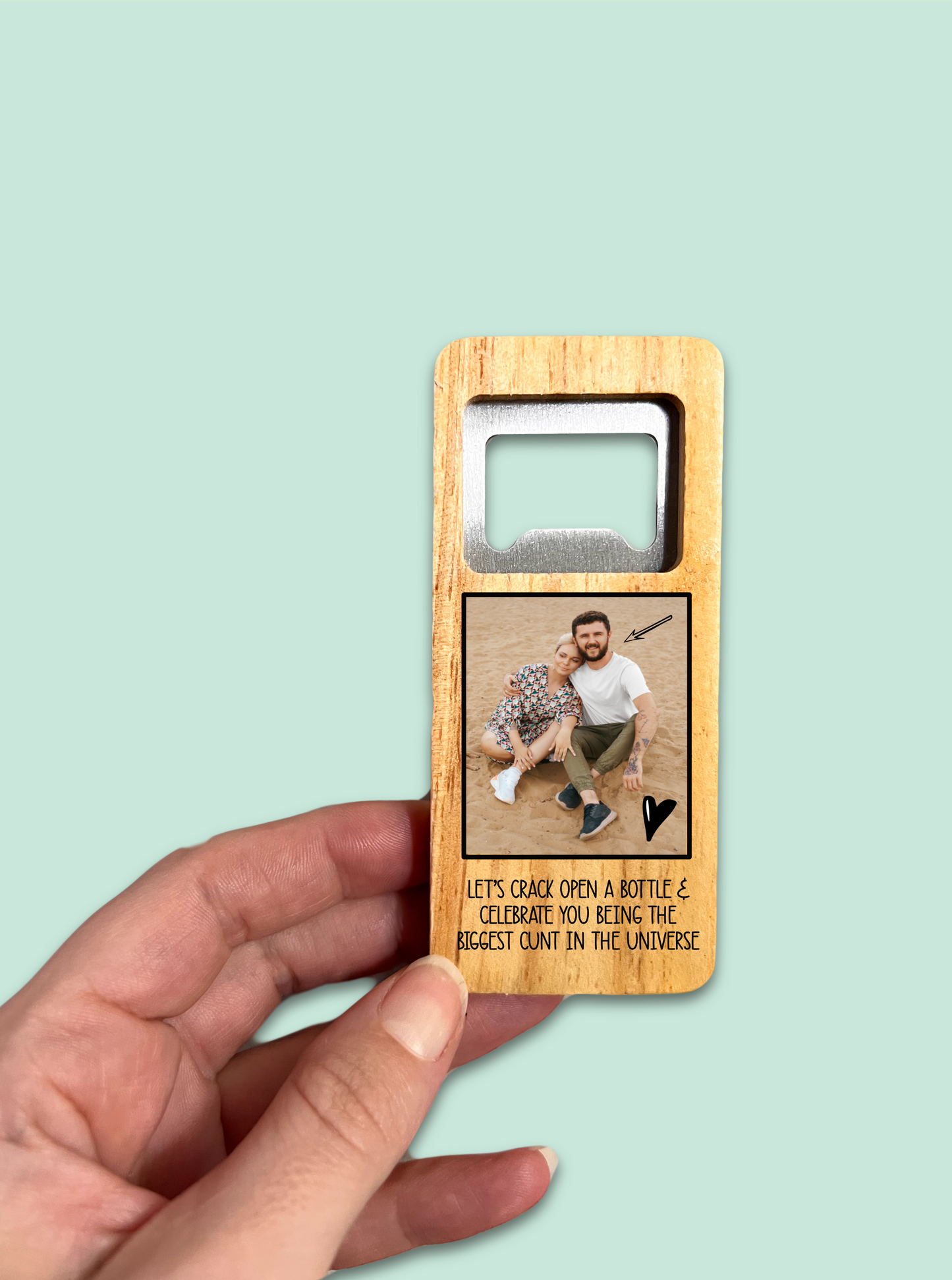 A 10cm wooden rectangle handle with a personalised photo printed to the front. Under the photo it has a funny quote 'let's crack open a bottle & celebrate you being the biggest c*nt in the universe'. To the top is a durable stainless steel opener.