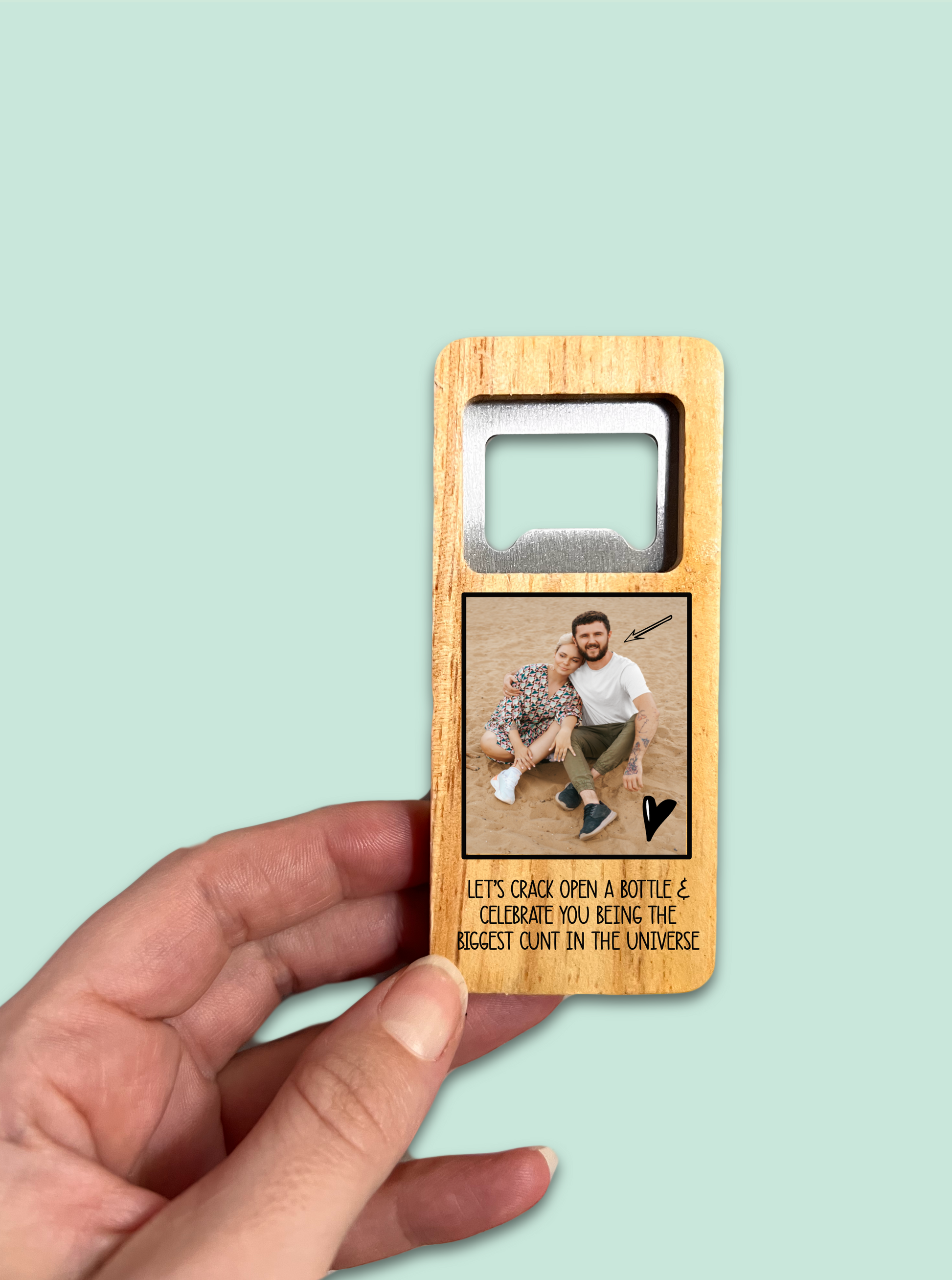 A 10cm wooden rectangle handle with a personalised photo printed to the front. Under the photo it has a funny quote 'let's crack open a bottle & celebrate you being the biggest c*nt in the universe'. To the top is a durable stainless steel opener.