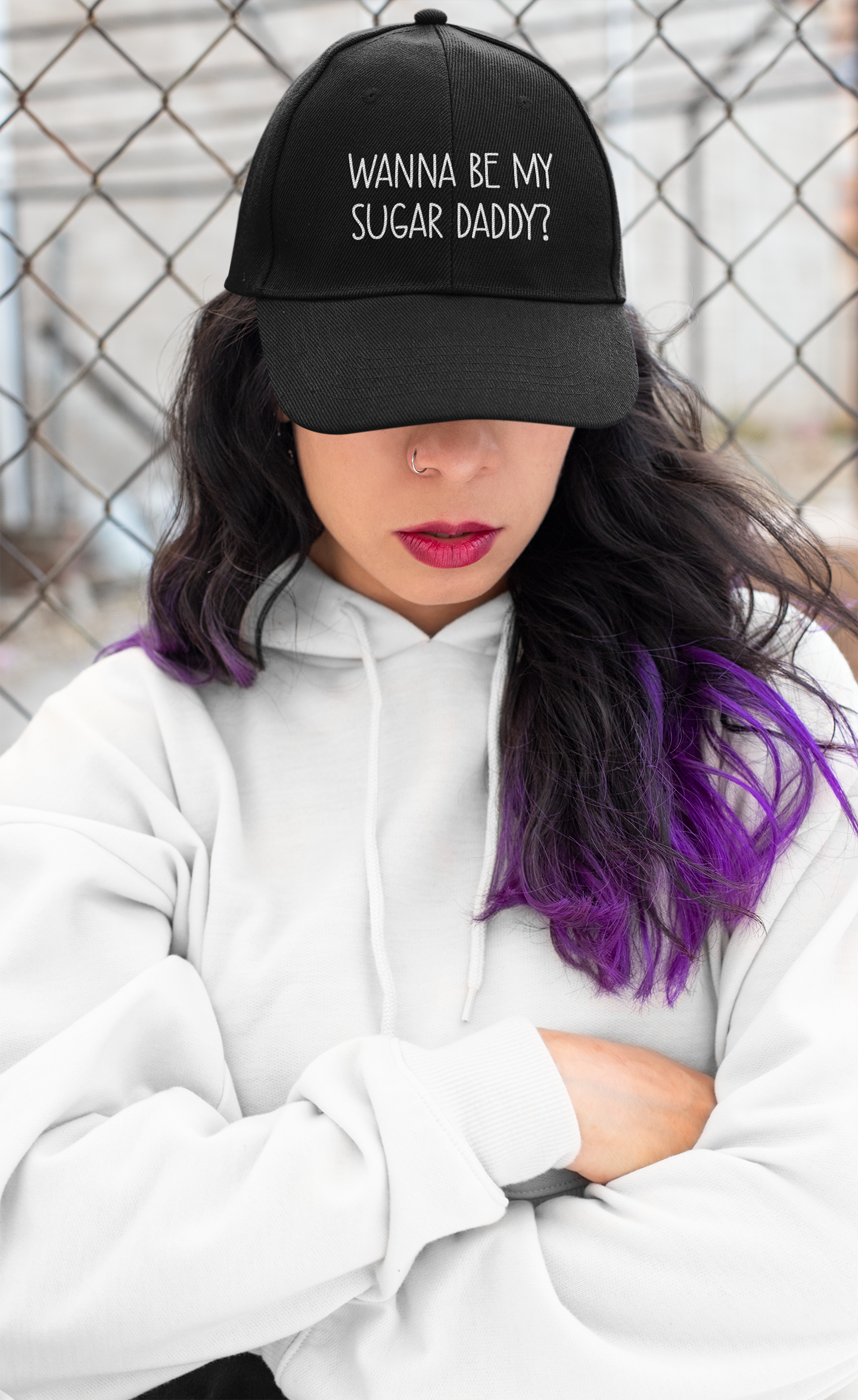 A lady wearing a black cotton cap with white lettering to the front which reads 'wanna be my sugar daddy?'.