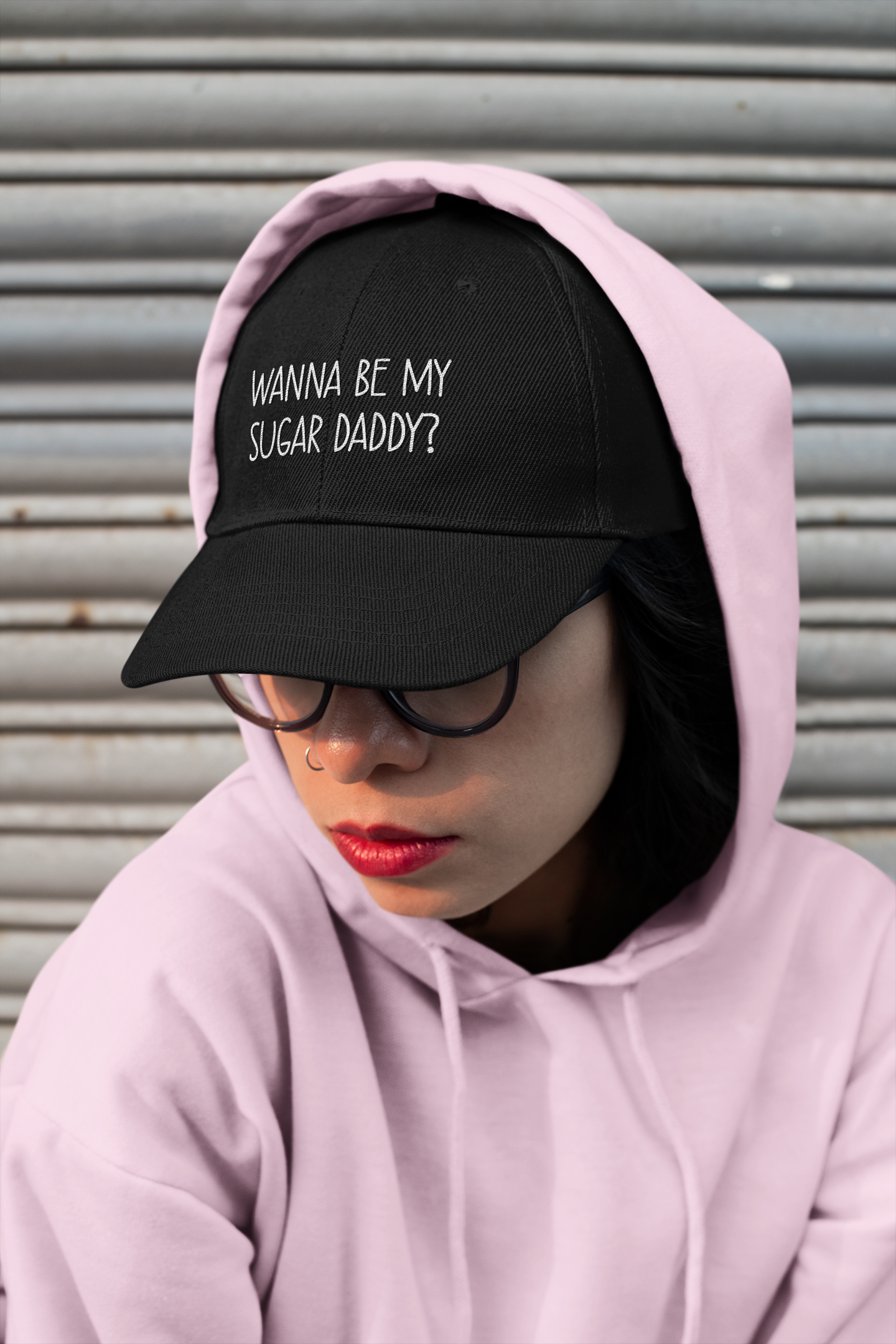 A lady wearing a black cotton cap with white lettering to the front which reads 'wanna be my sugar daddy?'.