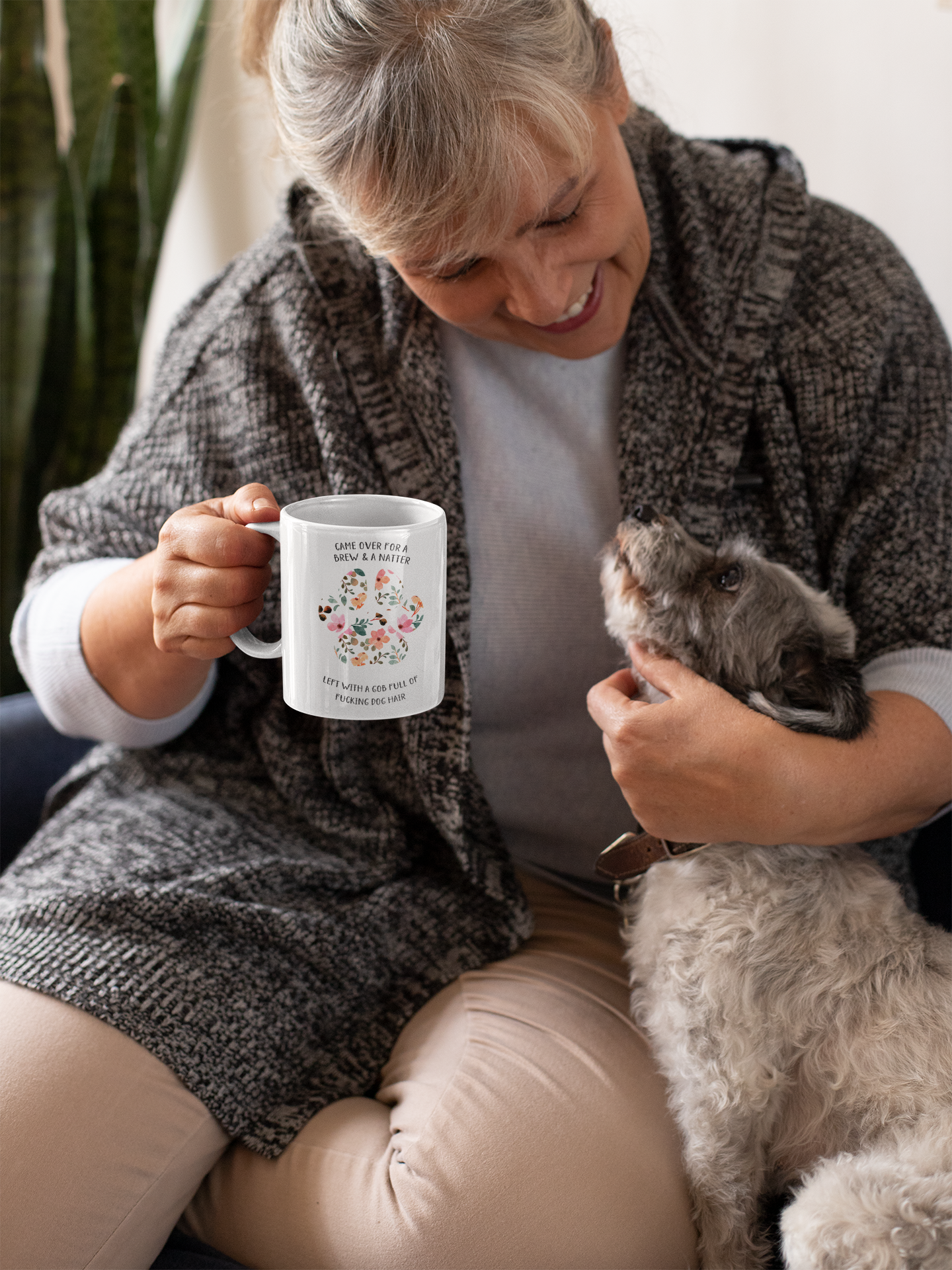 White ceramic mug with a cute colourful floral dog paw print design. To the top of the print it reads 'came over for a brew & a natter' then to the bottom is says 'left with a gob full of fucking dog hair'. Printed in black ink.