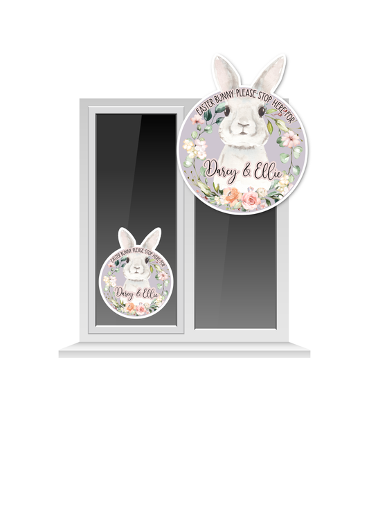 Window cling sticker featuring a water colour bunny design, surrounded by a floral sprint wreath. At top it says ' Easter bunny please stop here for' and to the bottom has 2 children's names as personalisation. 