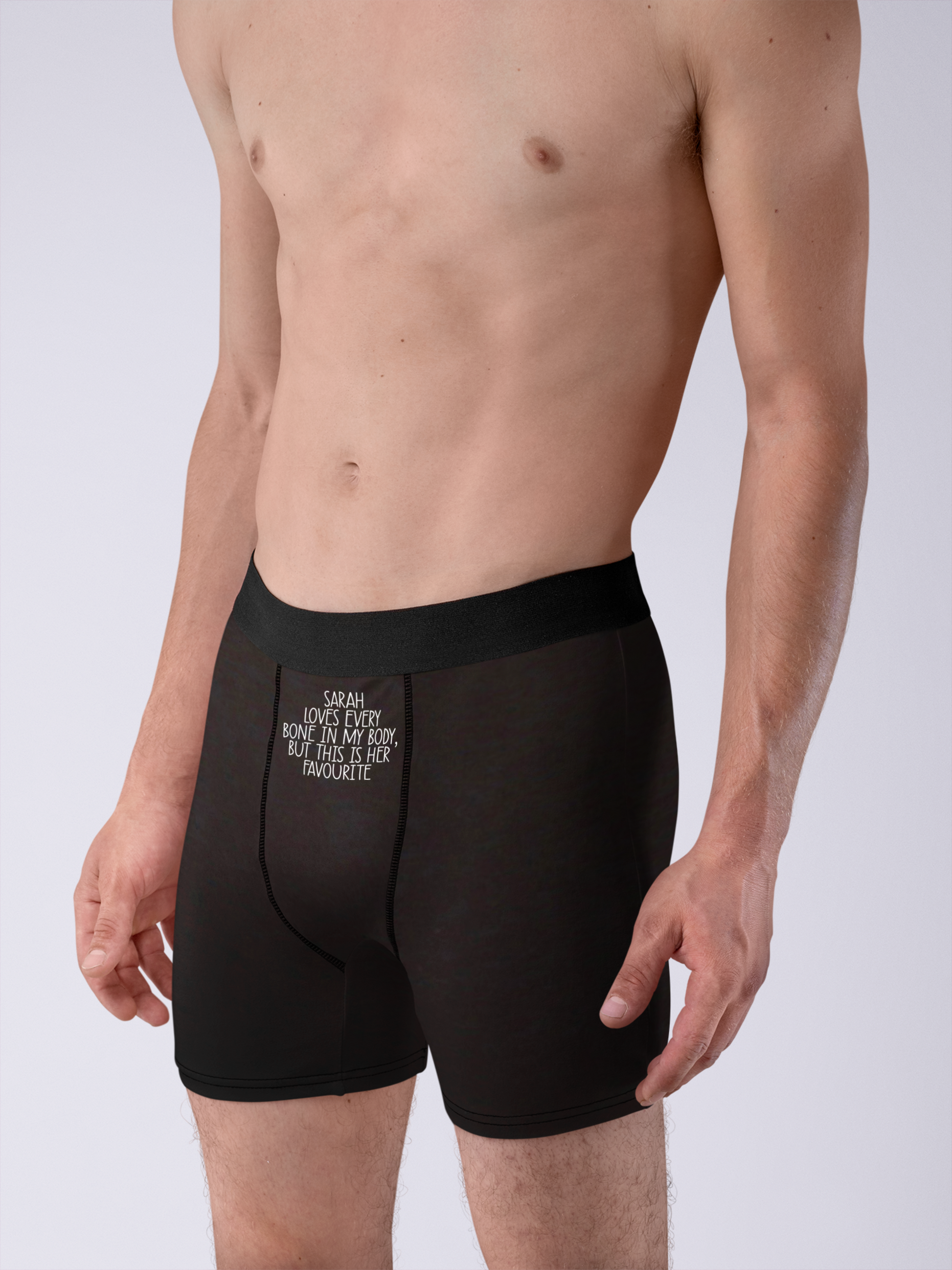 Black pair of mens boxer short pants with a white funny quote to the top middle section. It reads '(name) loves every bone in my body... but this is her favourite'.