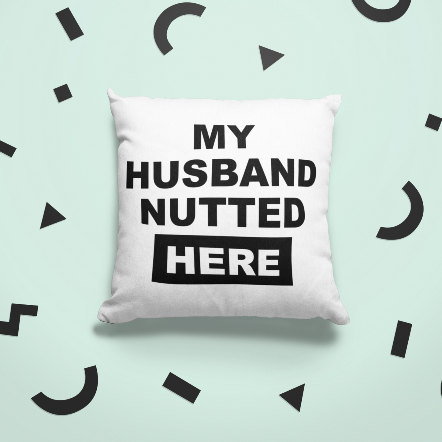 White, square cushion with bold text to the front saying 'my husband nutted here'.