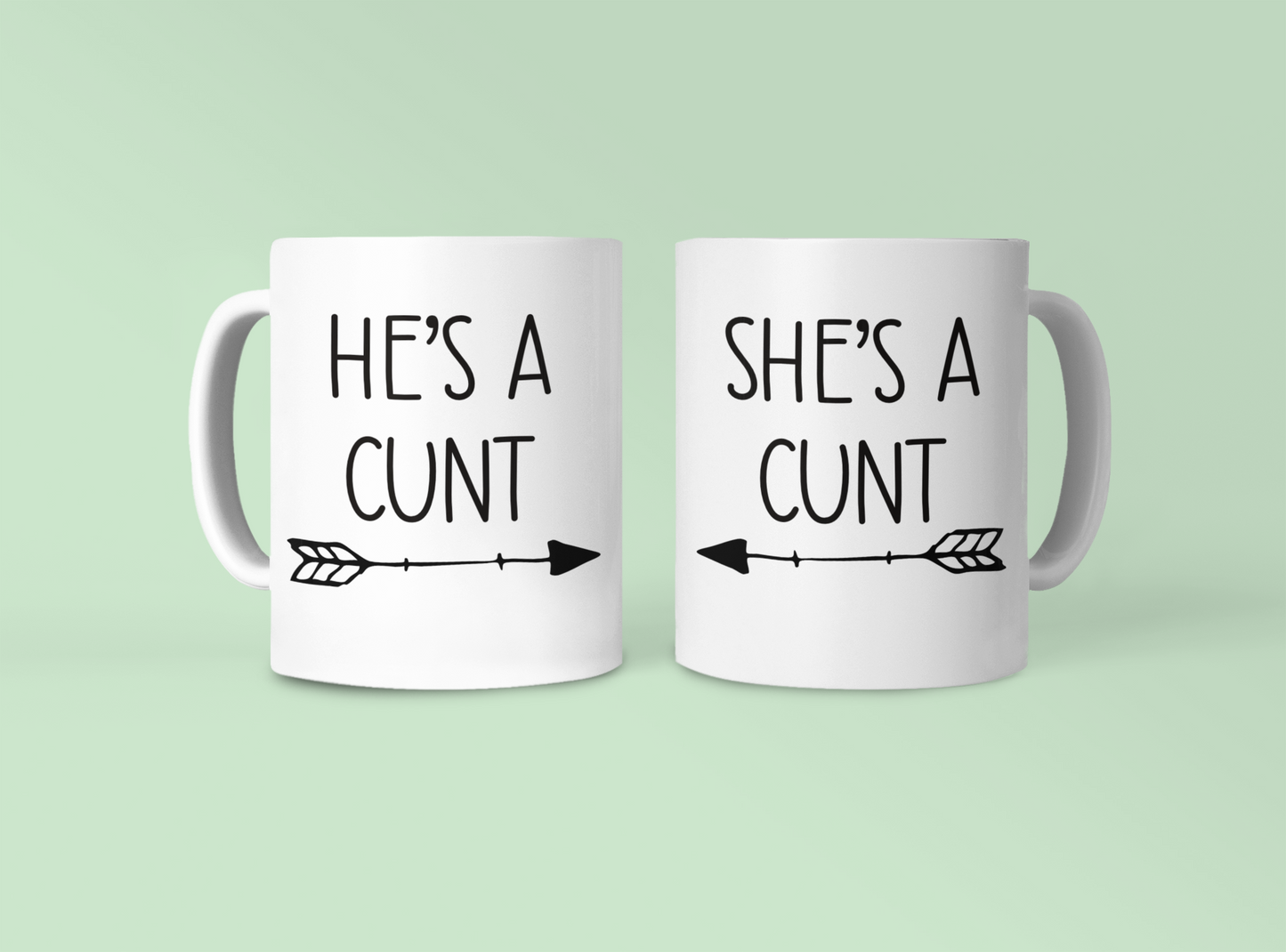 A pair of white ceramic mugs. One has 'he's a c*nt' with an arrow underneath pointing to the right. The other has 'she's a c*nt' with the arrow pointing to the left. Both printed to the front in black ink.