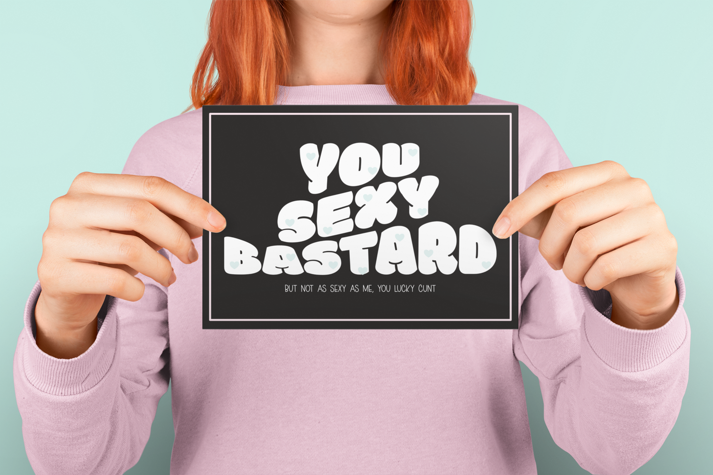 Black horizontal greetings card with a fun quote saying 'you sexy bastard' in a bold font. Underneath is a smaller font which reads 'but not as sexy as me, you lucky c*nt.