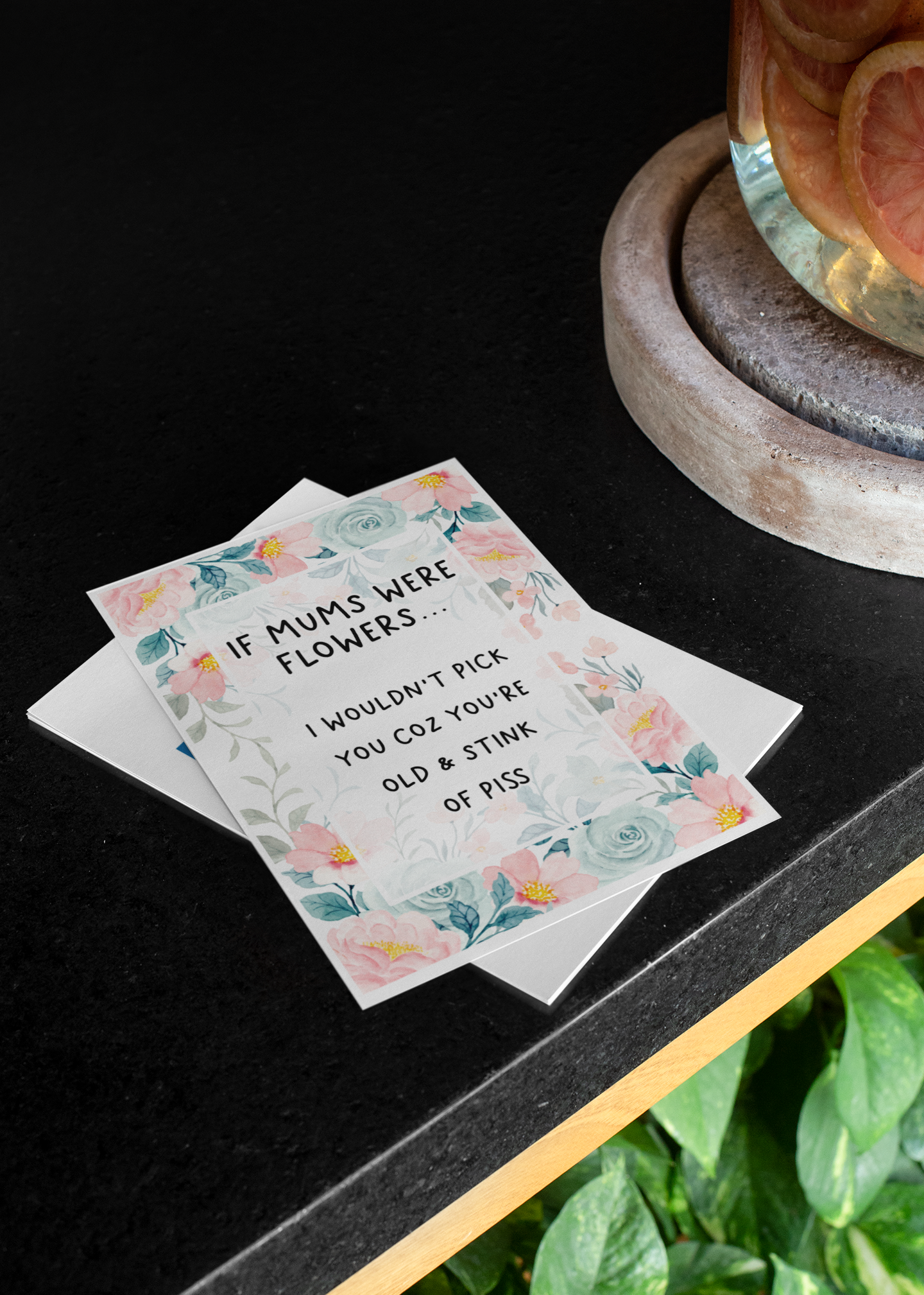 Greetings card with a pastel colour floral design to the front with the quote 'if mums were flowers... i wouldn't pick you coz you're old & stink of piss' printed in the middle in black ink. 