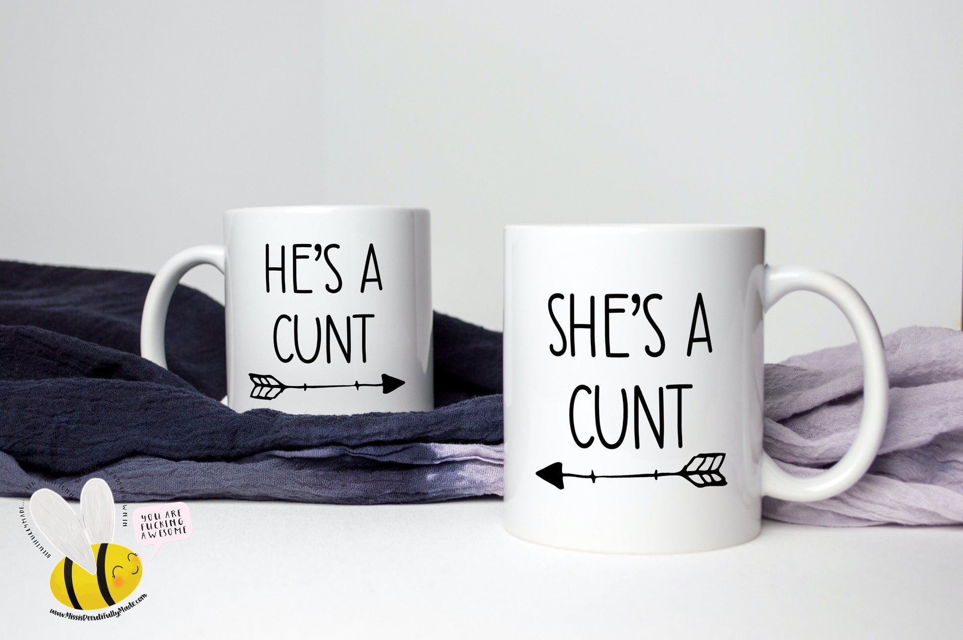 A pair of white ceramic mugs. One has 'he's a c*nt' with an arrow underneath pointing to the right. The other has 'she's a c*nt' with the arrow pointing to the left. Both printed to the front in black ink.