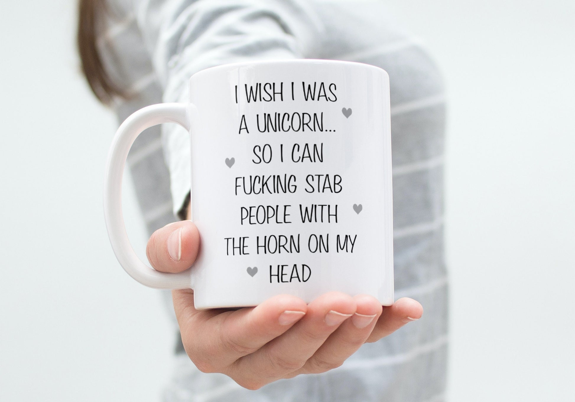 A white ceramic mug featuring the funny quote ‘I wish i was a unicorn... So i can fucking stab people with the horn on my head’. Printed in black ink with little grey hearts surround the text.