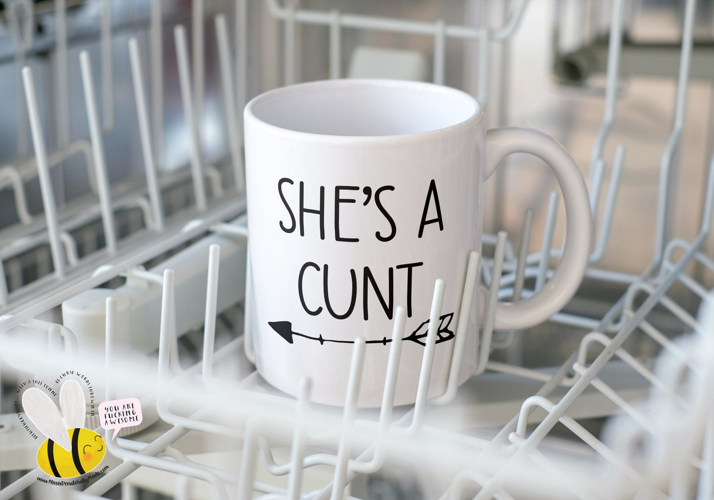 A white ceramic mug featuring the funny quote 'she's a c*nt' with an arrow pointing to the left. Printed to the front in black ink.