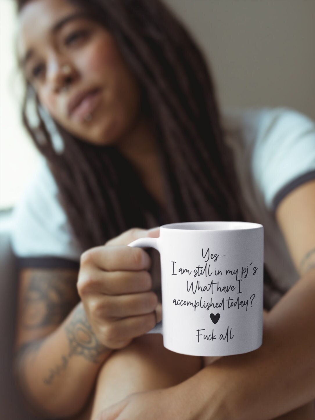 A white ceramic mug featuring the funny quote ‘yes i'm still in my pj's. What have i accomplished today? Fuck all’. Printed in black ink with a black heart.