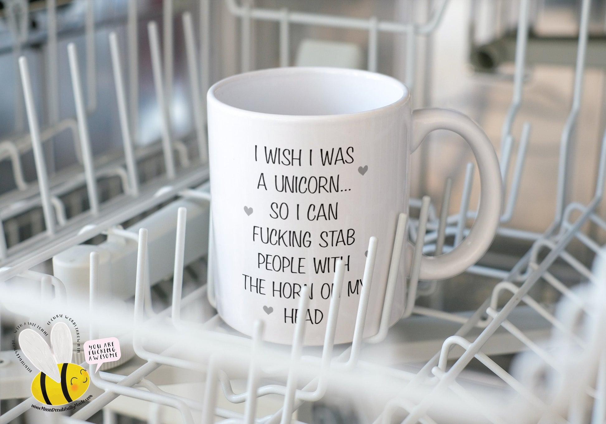 A white ceramic mug featuring the funny quote ‘I wish i was a unicorn... So i can fucking stab people with the horn on my head’. Printed in black ink with little grey hearts surround the text.