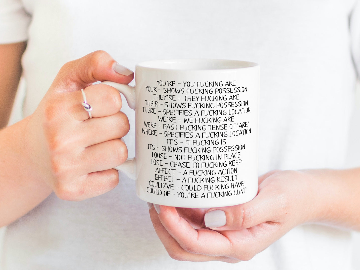 A white ceramic mug featuring funny spelling corrections such as You've - You fucking are and Your- shows fucking progression. Printed in black ink.