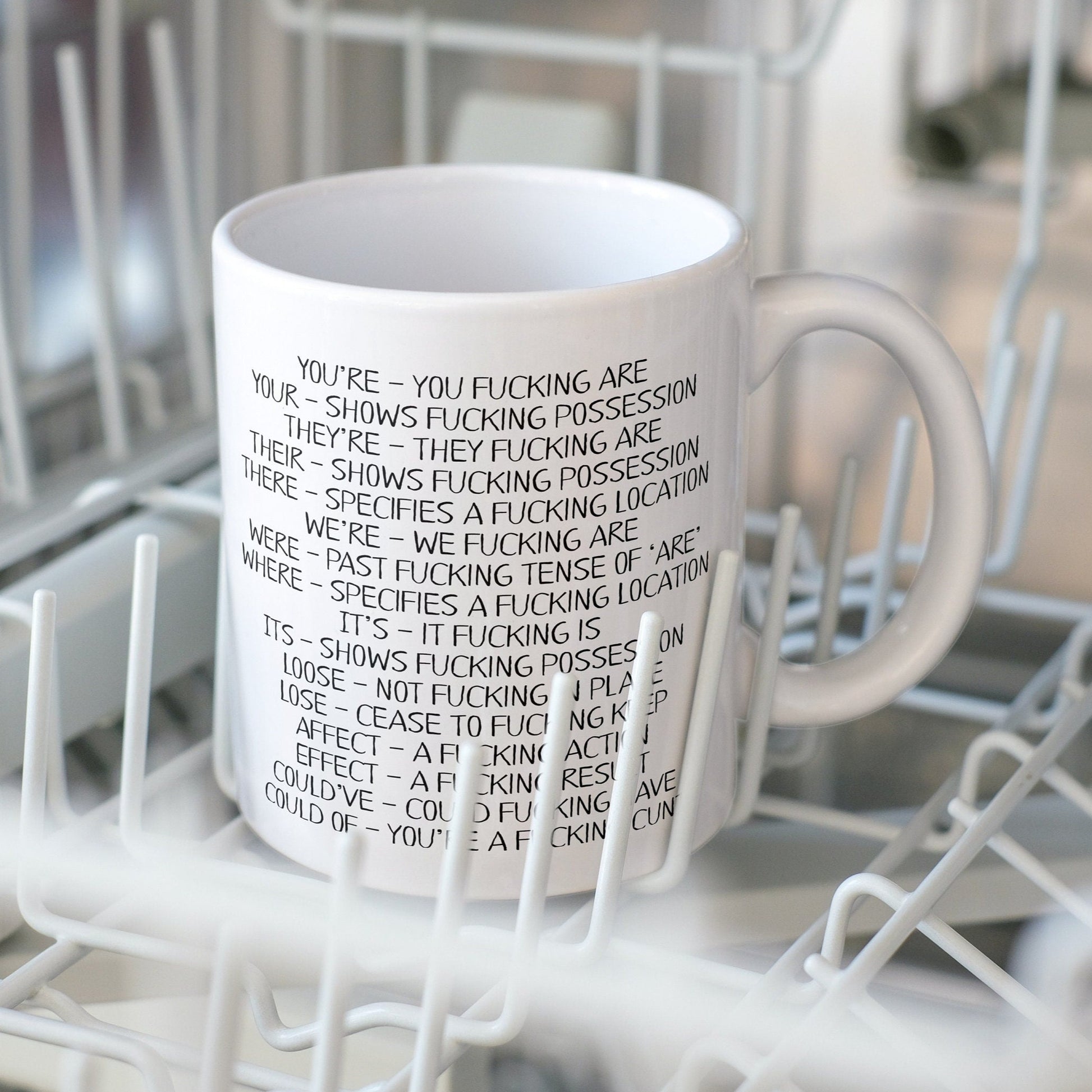 A white ceramic mug featuring funny spelling corrections such as You've - You fucking are and Your- shows fucking progression. Printed in black ink.