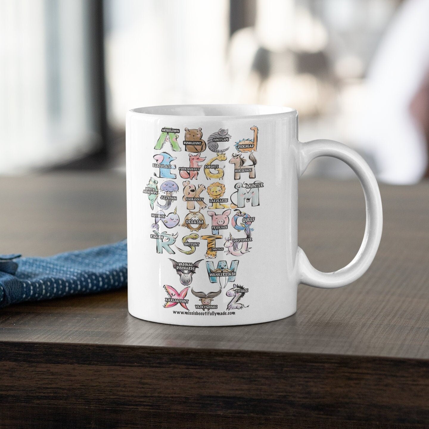 A white ceramic mug with a pink handle, featuring a fun, colourful, animal alphabet. A is for arseclown, B is for bunglec*nt etc.