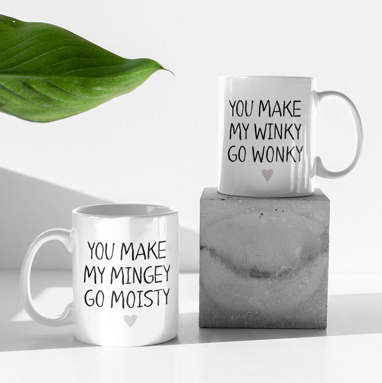 A pair of white ceramic mug featuring the funny quotes you make my mingey go moisty and you make my winky go wonky. Printed in black ink with a grey heart to the bottom centre of the design.