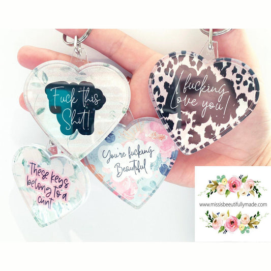 4 acrylic heart keyrings with various designs. Some examples of the quotes are 'fuck this shit', i fucking love you' and 'you're fucking beautiful'.