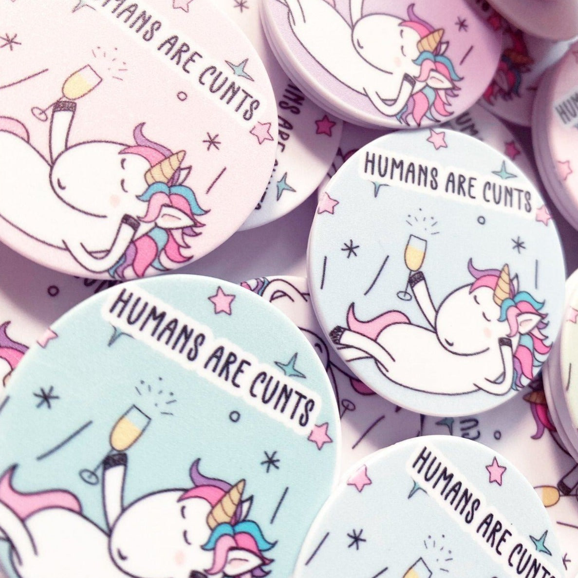 A round phone case popper with a cute stars & unicorn design to the front & the quote 'humans are c*nts' to the top.