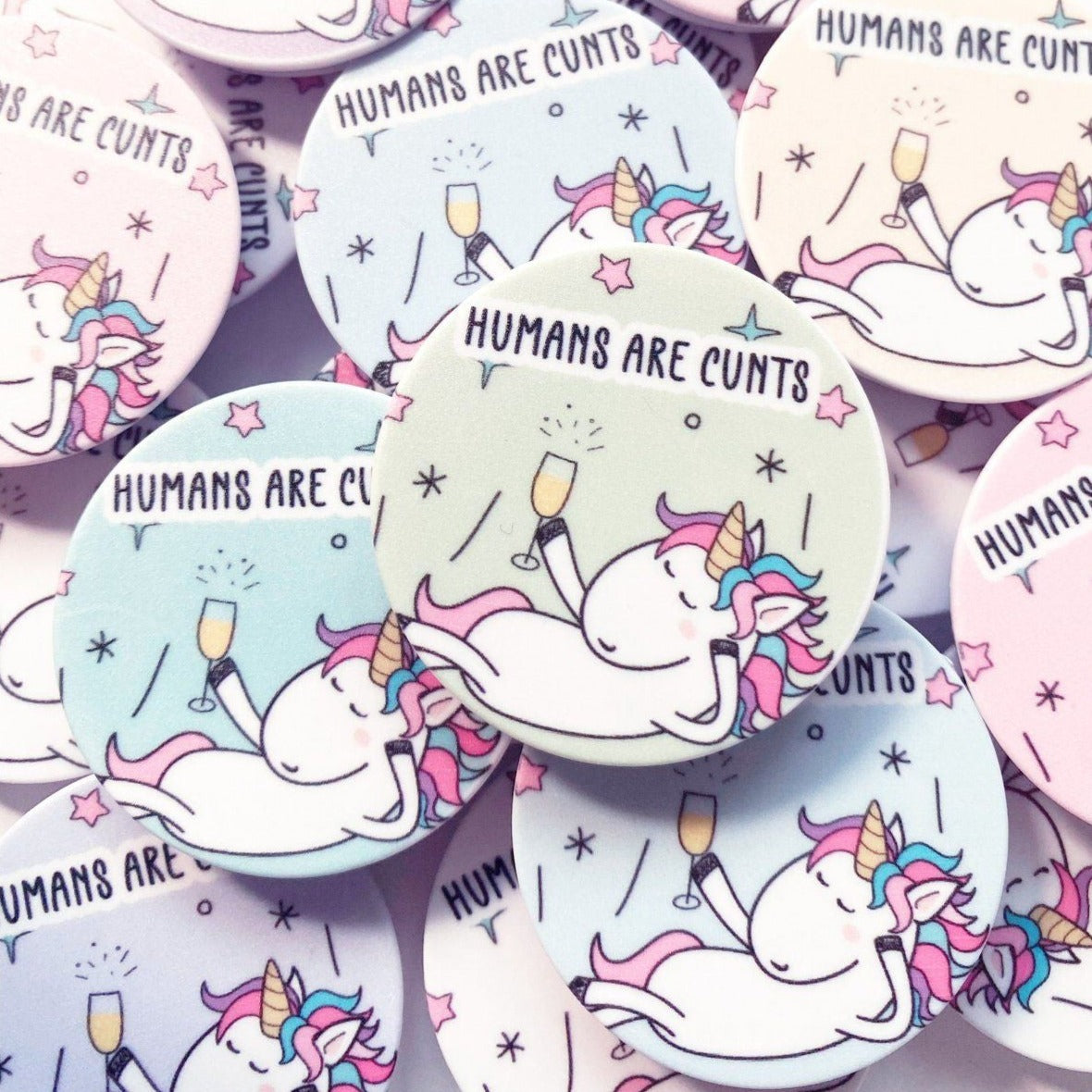 A round phone case popper with a cute stars & unicorn design to the front & the quote 'humans are c*nts' to the top.