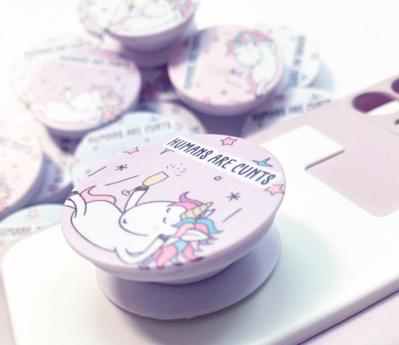 A round phone case popper with a cute stars & unicorn design to the front & the quote 'humans are c*nts' to the top.