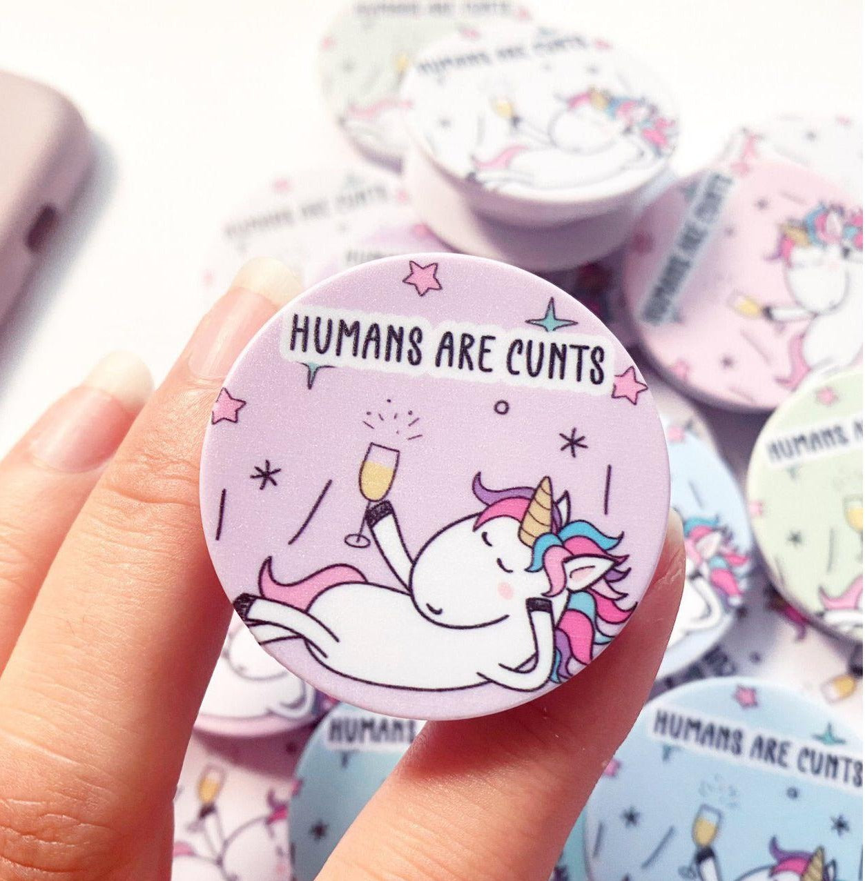 A round phone case popper with a cute stars & unicorn design to the front & the quote 'humans are c*nts' to the top.