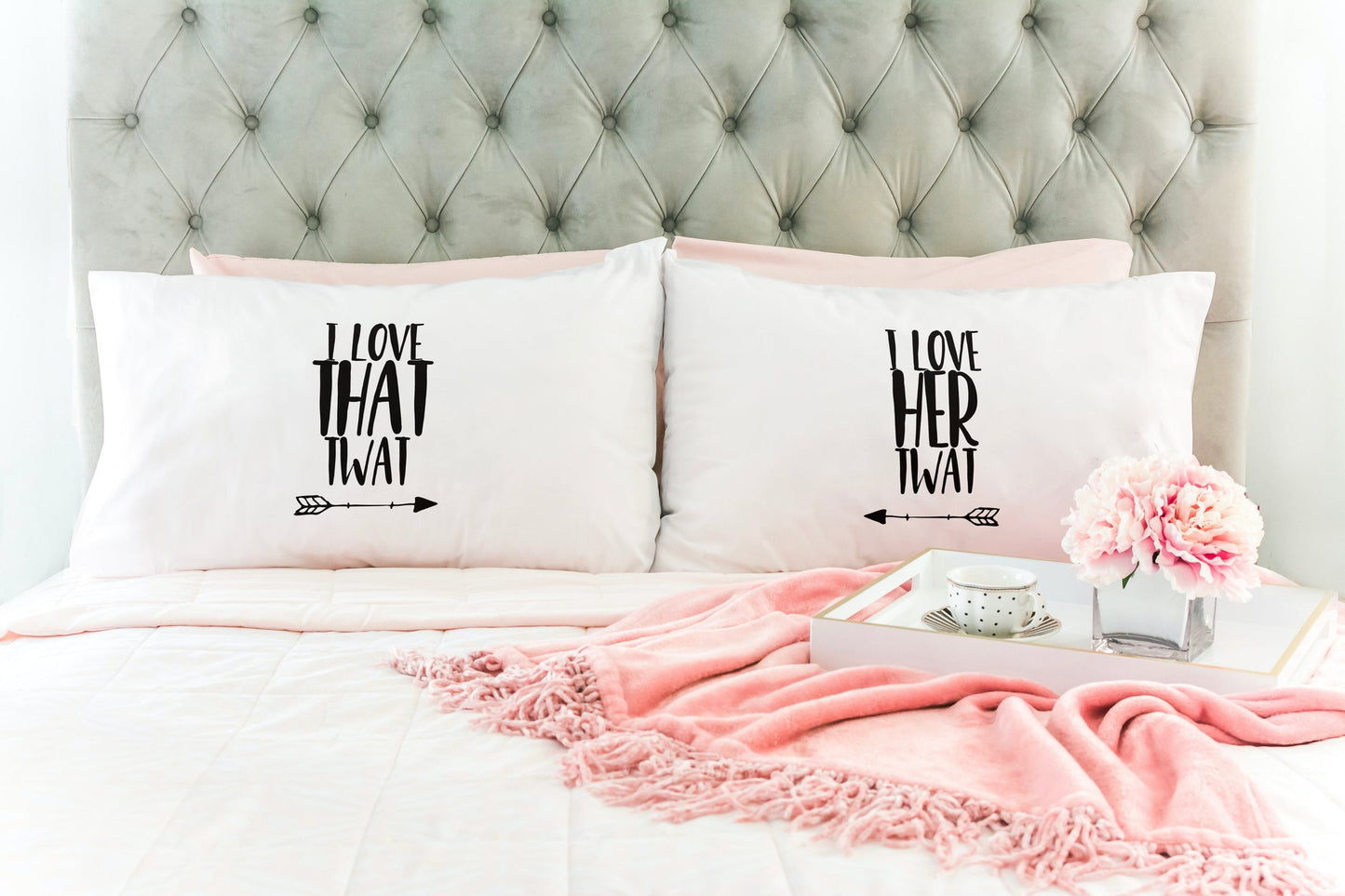 White pair of pillow cases on a made up bed, featuring funny quotes. The left reads 'i love that twat' with an arrow pointing to the right. The other pillow reads 'i love her twat' with an arrow pointing to the left.