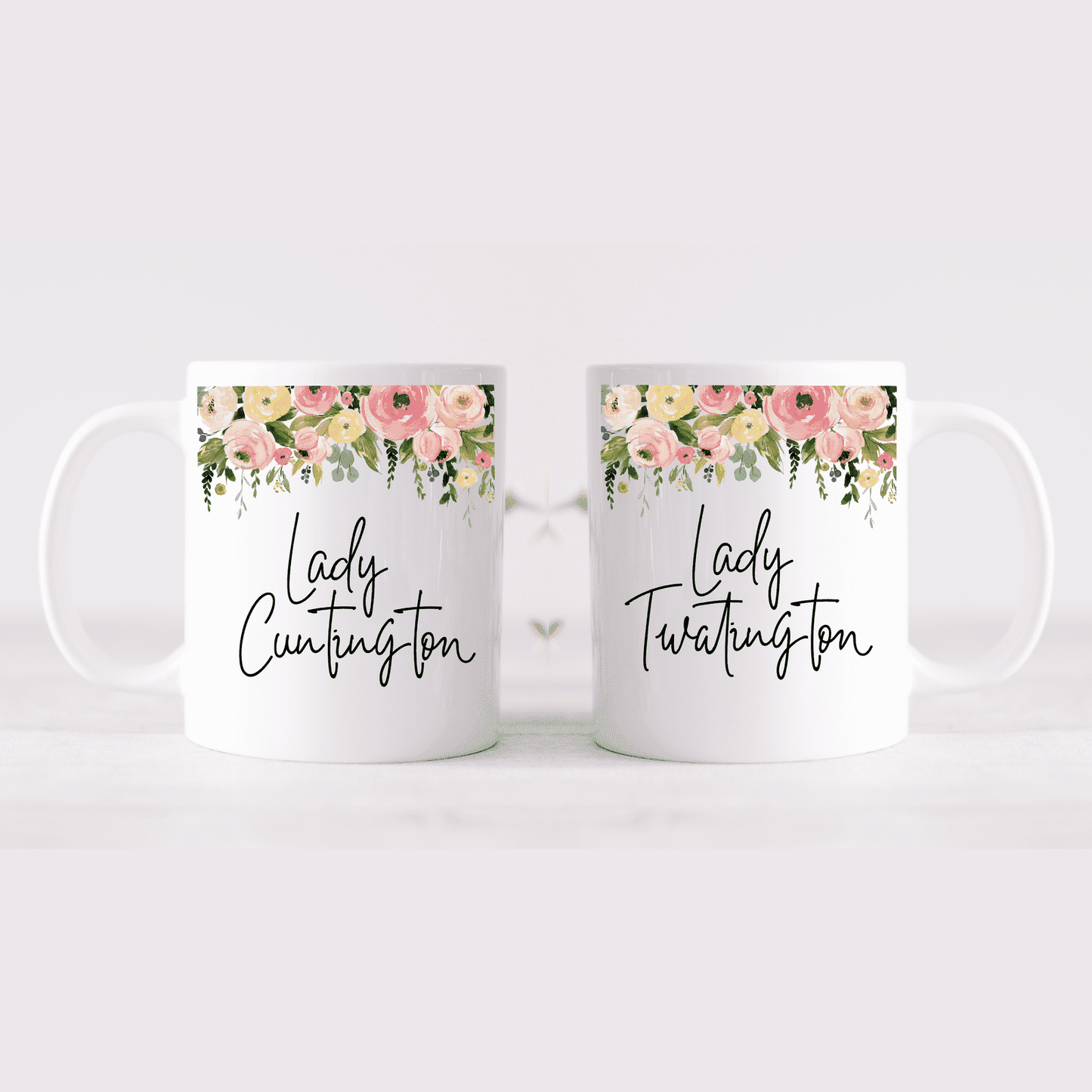 A pair of white mugs with a colourful floral design to the top. In the middle has the quotes 'lady c*ntington' and 'lady twatington'. Printed in black ink.