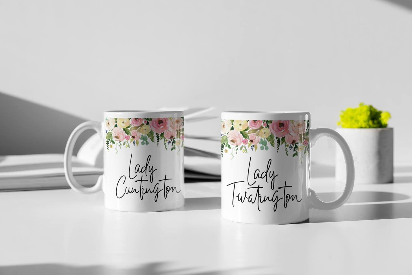 Two white mugs with a colourful floral border to the top. Underneath is the quote lady cuntington on one and lady twatington on the other.