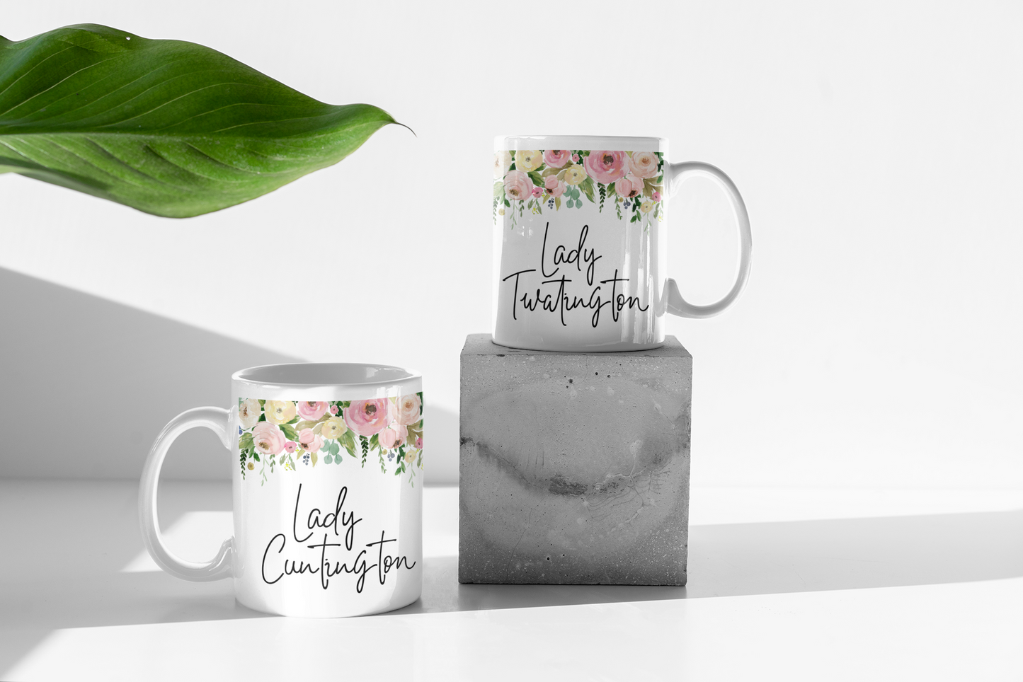 Two white mugs with a colourful floral border to the top. Underneath is the quote lady cuntington on one and lady twatington on the other.