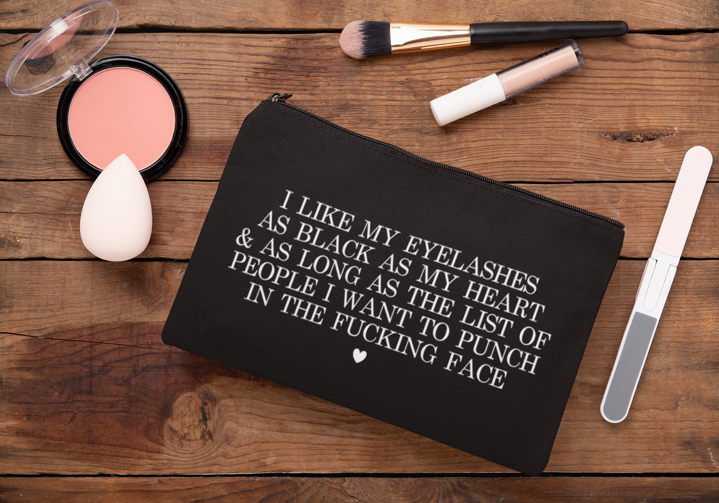 Black cosmetic bag featuring a funny quote in a bold text which reads 'i like my eyelashes as black as my heart & as long as the list of people i want to punch in the fucking face.' Printed in white.