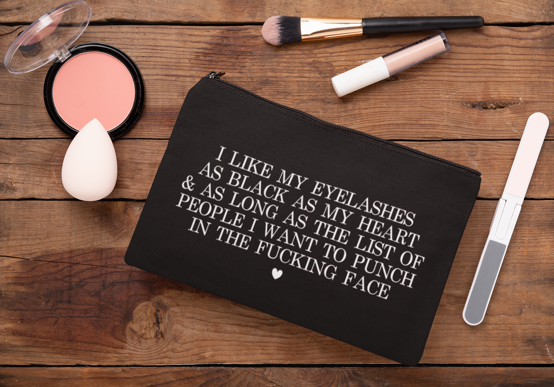 Black cosmetic bag featuring a funny quote in a bold text which reads 'i like my eyelashes as black as my heart & as long as the list of people i want to punch in the fucking face.' Printed in white.