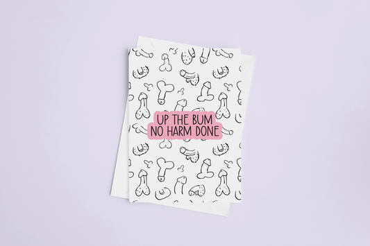 A white folded greetings card & envelope featuring a fun willy design print to the front. Over the print is a funny quote 'up the bum, no harm done', printed in black & pink ink