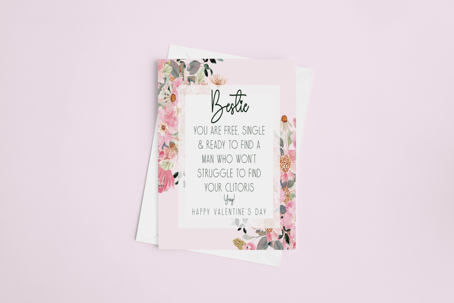 White card with a pink floral design to the front. In the middle has a funny message that reads 'bestie, you are single & ready to find a man who won't struggle to find your clitoris. Yay, happy valentine's day'. Printed in black ink.