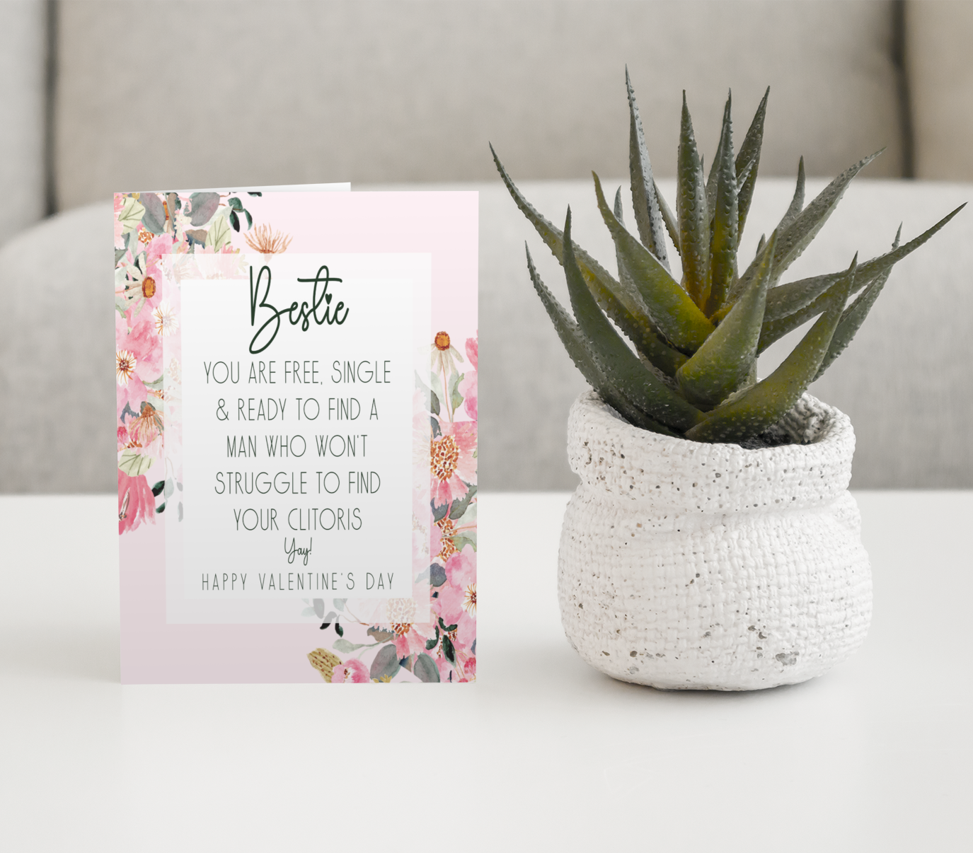 White card with a pink floral design to the front. In the middle has a funny message that reads 'bestie, you are single & ready to find a man who won't struggle to find your clitoris. Yay, happy valentine's day'. Printed in black ink.