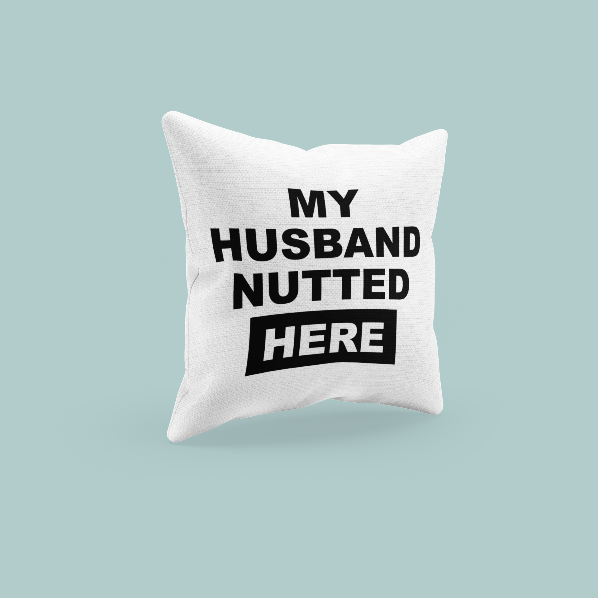 White, square cushion with bold text to the front saying 'my husband nutted here'. 